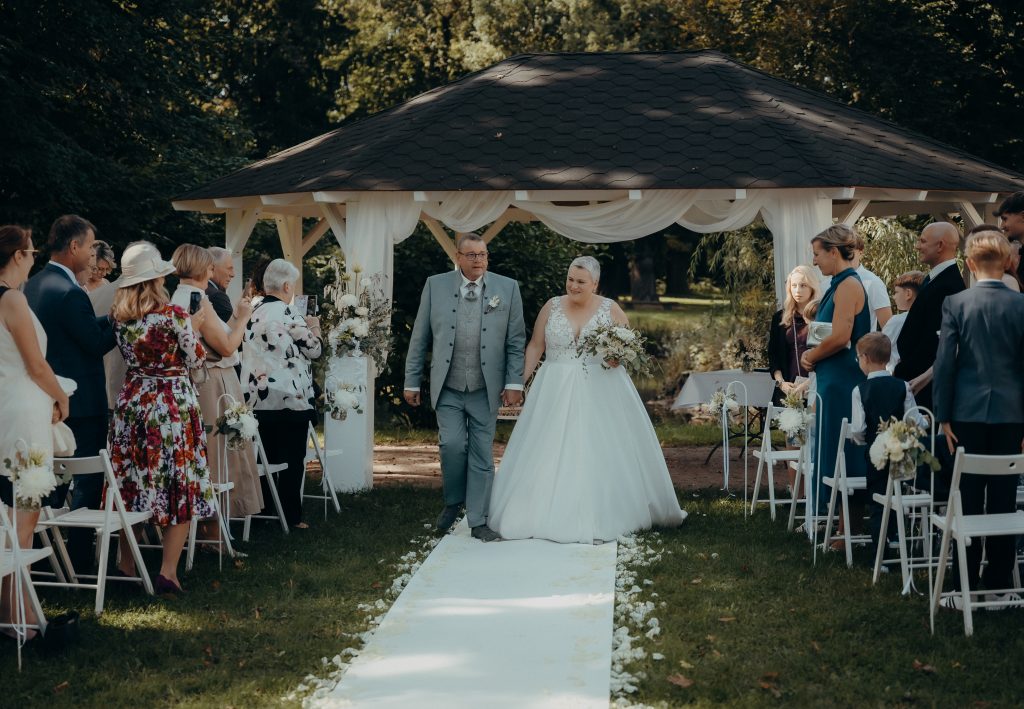 Hochzeit im Freien, Brautpaar und Gäste feiern bei schönem Wetter unter einem festlichen Pavillon.